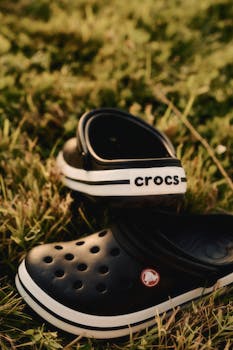 Captivating close-up of black Crocs resting on a grassy field, showcasing casual footwear style.