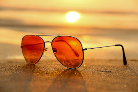 Close-up of sunglasses on a beach during a vibrant sunset, capturing the essence of summer.